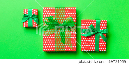 wrapped Christmas or other holiday handmade present in paper with green ribbon on green background. Present box, decoration of gift on colored table, top view 69725969