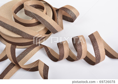 Brown beige Cotton ribbon, roll textilies on bobbin. strapping tape with curl on white backgroud. 69726078