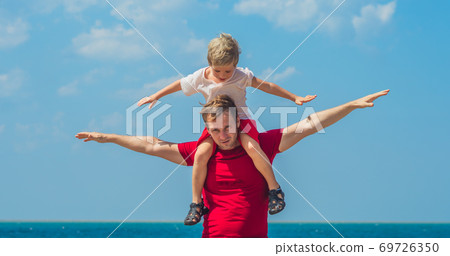 Happy smile father hugs holds on shoulders son boy male child stand blue lazur sea panorama skyline horizon in sunshine day clear sky, play show outstretched hands like airplane. Travel, relationship Happy smile father hugs holds on shoulders son boy male child stand blue lazur sea panorama skyline horizon in sunshine day clear sky, play show outstretched hands like airplane. Travel, relationship 69726350
