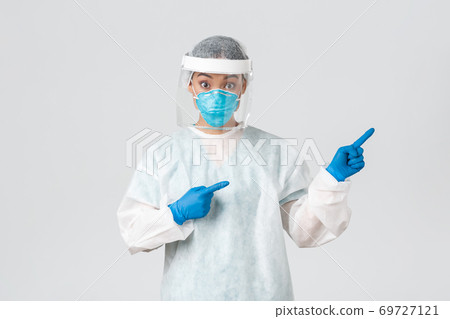 Covid-19, coronavirus disease, healthcare workers concept. Surprised and intrigued asian female doctor, tech lab employee in personal protective equipment look amazed and pointing fingers right 69727121
