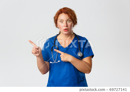 Medicine, healthcare and coronavirus concept. Portrait of shocked and impressed redhead female doctor, nurse in scrubs pointing fingers left, asking question, interested in banner, grey background 69727141