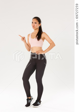 Sport, gym and healthy body concept. Full length of skeptical and displeased female athlete, asian sportswoman sulking and frowning disappointed, pointing finger upper left corner and complaining Sport, gym and healthy body concept. Full length of skeptical and displeased female athlete, asian sportswoman sulking and frowning disappointed, pointing finger upper left corner and complaining 69727259