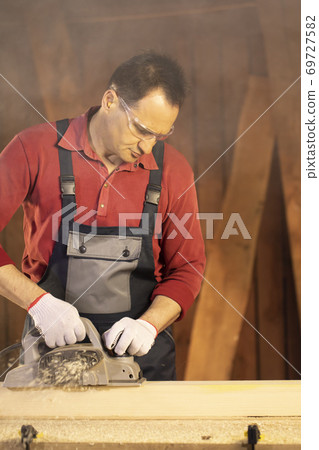 middle-aged male carpenter in googles working on workbench with electric planer middle-aged male carpenter in googles working on workbench with electric planer 69727582