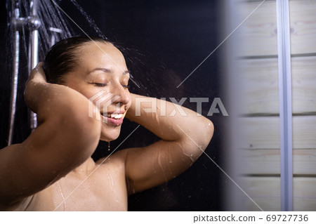 Happy beautiful woman standing under stream of water in bathroom, taking shower 69727736