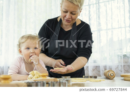 Smiling cute baby eating raw ginger cookie dough in the kitchen with grandmother 69727844