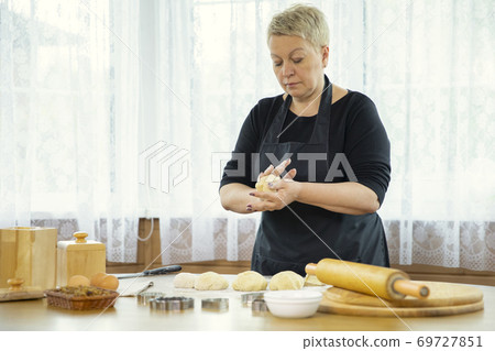 Caucasian housewife forms cakes from raw dough on a table sprinkled with flour 69727851