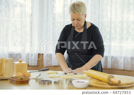 Caucasian housewife sculpts raw dough with her hands on a table with flour. Caucasian housewife sculpts raw dough with her hands on a table with flour. 69727853