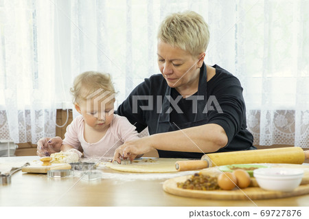 Smiling cute baby girl kneading dough for cookies in kitchen at a wooden table. Smiling cute baby girl kneading dough for cookies in kitchen at a wooden table. 69727876