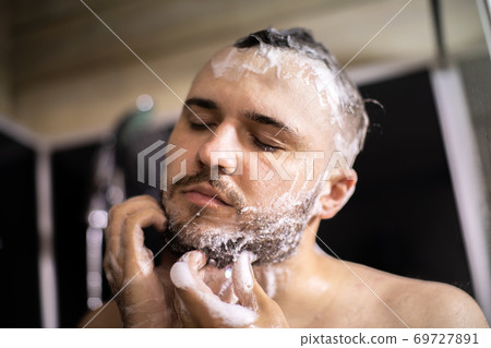 young bearded naked brunette man washes his beard with shampoo foam young bearded naked brunette man washes his beard with shampoo foam 69727891