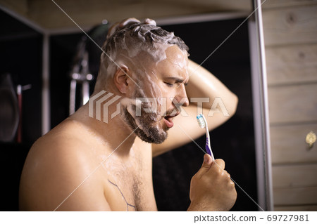 Attractive young man in foam having fun while taking shower, singing in bathroom 69727981