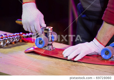 Men's hand fixing red plastic skateboard in home workshop with socket wrench Men's hand fixing red plastic skateboard in home workshop with socket wrench 69728060