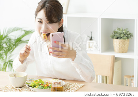 一個女人一邊吃一邊看著智能手機 69728263