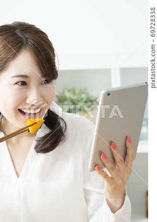 一個女人一邊看著平板電腦一邊吃飯 一個女人一邊看著平板電腦一邊吃飯 69728338