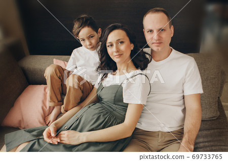A family with two children is sitting on the sofa. Weekend at home. Spending time together. Love and peace at home A family with two children is sitting on the sofa. Weekend at home. Spending time together. Love and peace at home 69733765