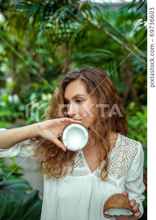 Woman in white dress with coconut in her hands looking thoughtful 69736603