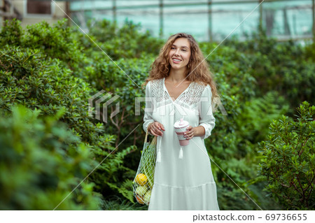 Woman in white dress with bags of vegetables in a greenhouse Woman in white dress with bags of vegetables in a greenhouse 69736655