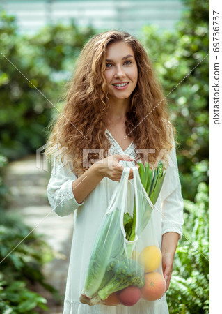 Woman in white dress holding a bag with veggies Woman in white dress holding a bag with veggies 69736737