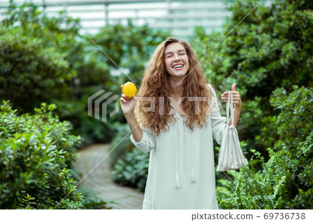 Woman in white dress holding a lemon and looking happy Woman in white dress holding a lemon and looking happy 69736738