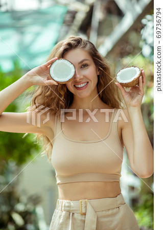 Pretty young long-haired woman holding a coconut and looking cheerful Pretty young long-haired woman holding a coconut and looking cheerful 69736794