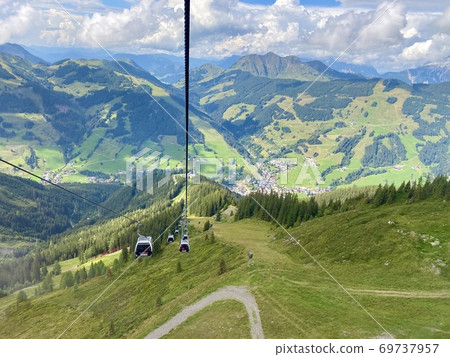 Aerial view on Saalbach village and mountains in Saalbach-Hinterglemm skiing region in Austria on a beautiful summer day from cableway on the village with holiday ressorts, the church and other Aerial view on Saalbach village and mountains in Saalbach-Hinterglemm skiing region in Austria on a beautiful summer day from cableway on the village with holiday ressorts, the church and other 69737957