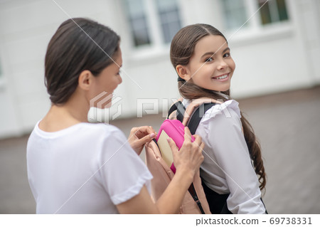 Mom zipping her daughters school backpack and smiling Mom zipping her daughters school backpack and smiling 69738331