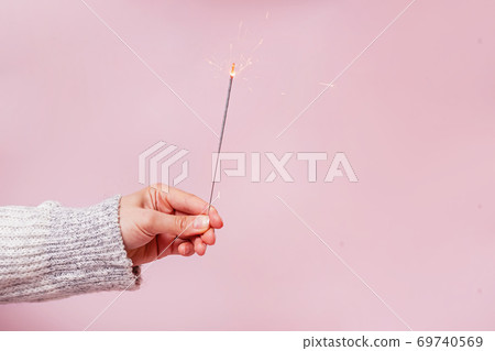 Female hand in sweater holding festive Christmas sparkler Female hand in sweater holding festive Christmas sparkler 69740569