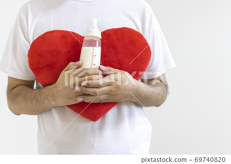 A man holding a baby bottle and a heart cushion 69740820