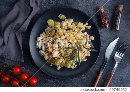 Stewed chicken minced meat with vegetables zucchini pepper spices on a black plate. 69740983