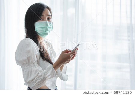 Asian woman wearing protective face mask, and using mobile smart phone	 69741120