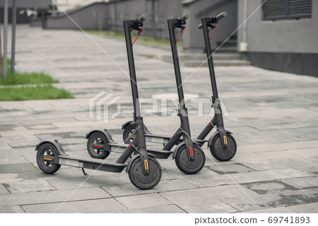 Three modern stylish black electric scooter are parked near big office centre. Electricity and eco friendly concept. Three modern stylish black electric scooter are parked near big office centre. Electricity and eco friendly concept. 69741893