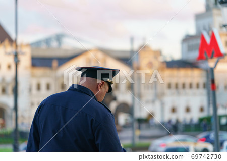 Policeman at the Moscow city street. He wear blue uniform. Old architecture. Red letter M - the sign on entrance into subway. Back / rear view. Policeman at the Moscow city street. He wear blue uniform. Old architecture. Red letter M - the sign on entrance into subway. Back / rear view. 69742730