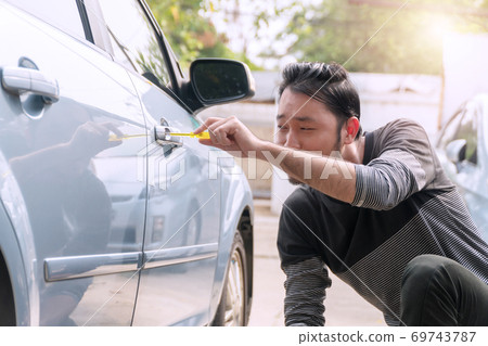 Thief male stealing secretly used screwdriver to open the car door in parking. Car robbery concept. Thief male stealing secretly used screwdriver to open the car door in parking. Car robbery concept. 69743787
