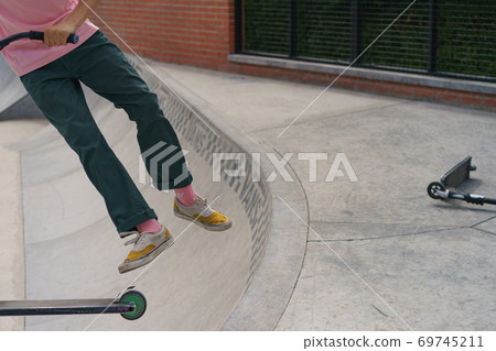 Teenager performs a trick on sportive push scooter on a city sports ground. He jumping over an obstacles. Extreme sports is very popular among youth. Teenager performs a trick on sportive push scooter on a city sports ground. He jumping over an obstacles. Extreme sports is very popular among youth. 69745211