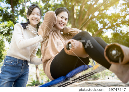 Beautiful asian woman practicing fitness,doing sit up exercise for health at city park,happy smiling female people doing abdominal sit ups in outdoor gym,mother,daughter enjoying and looking at camera 69747247