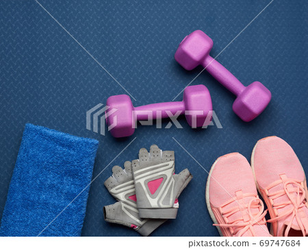 a pair of purple dumbbells, sports gloves and pink gym shoes on a blue neoprene mat a pair of purple dumbbells, sports gloves and pink gym shoes on a blue neoprene mat 69747684