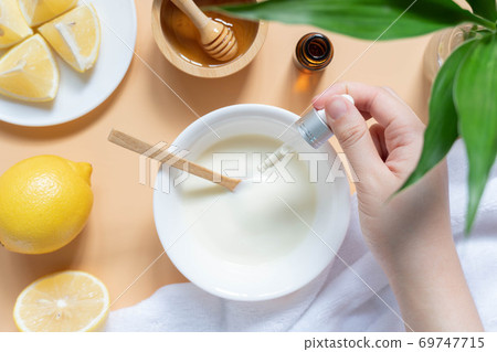 DIY natural face mask ingredients for bright and healthy skin. Woman hand holding cosmetic dropper w/ yogurt, lemon, honey and essential oil on wooden table. Beauty herbal skincare product concept. 69747715