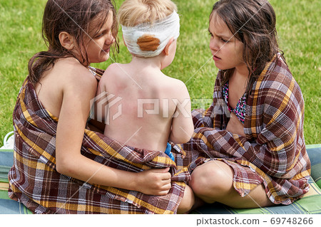 Two teenage girls feel sorry for little brother with bandaged head 69748266