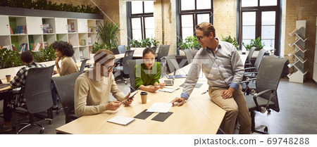 Sharing fresh ideas. Three young colleagues sitting at the desk in the modern coworking space, chatting and discussing new project, business people working together Sharing fresh ideas. Three young colleagues sitting at the desk in the modern coworking space, chatting and discussing new project, business people working together 69748288