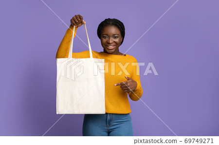 Cheerful Black Woman Holding And Pointing At Blank Textile Tote Shopping Bag 69749271