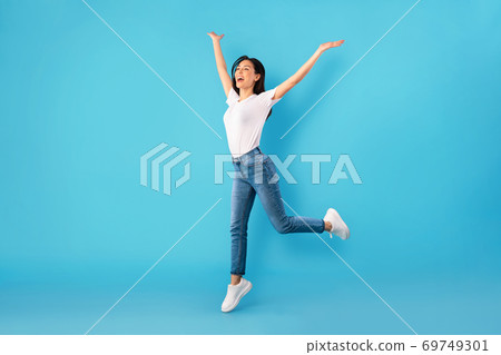 Happy woman jumping over blue studio wall Happy woman jumping over blue studio wall 69749301