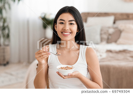 Happy asian woman holding bowl with homemade granola Happy asian woman holding bowl with homemade granola 69749304