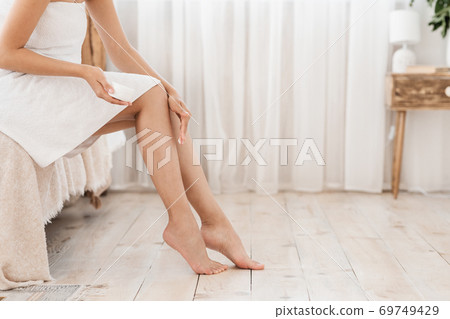 Cropped of unrecognizable woman sitting on bed, applying body lotion Cropped of unrecognizable woman sitting on bed, applying body lotion 69749429