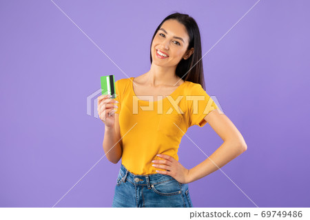 Woman holding credit card at pastel purple studio wall Woman holding credit card at pastel purple studio wall 69749486