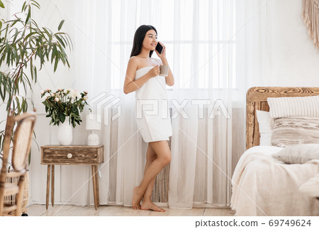 Relaxed asian woman drinking coffee and talking on phone Relaxed asian woman drinking coffee and talking on phone 69749624