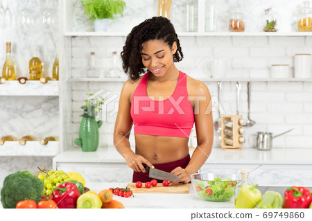 Beautiful young afro woman preparing vegetable salad at home Beautiful young afro woman preparing vegetable salad at home 69749860