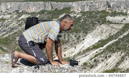 An adult man on the edge of the gorge, side view, is on all fours. Man over the gorge. 69749867