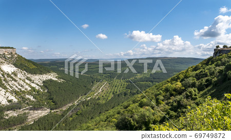 Landscape of a green plain in a mountainous gorge. White slopes of steep mountains. Landscape of a green plain in a mountainous gorge. White slopes of steep mountains. 69749872