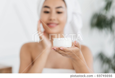 Happy asian woman wrapped in towel using face cream Happy asian woman wrapped in towel using face cream 69749898