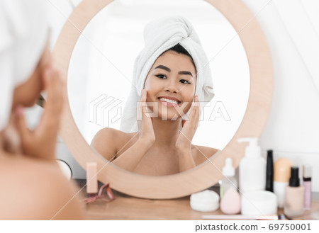Joyful asian young woman applying beauty product 69750001