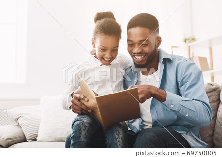 Happy evening. Afro dad reading fairy tale to his daughter Happy evening. Afro dad reading fairy tale to his daughter 69750005